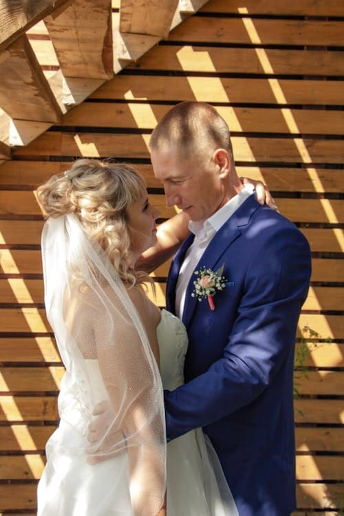 Bride and groom sharing an intimate moment outdoors against wooden backdrop.