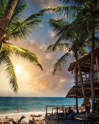 A beautiful tropical beach at sunset with lush palm trees and a rustic-chic beach bar, representing a luxury destination wedding locale in Riviera Maya.