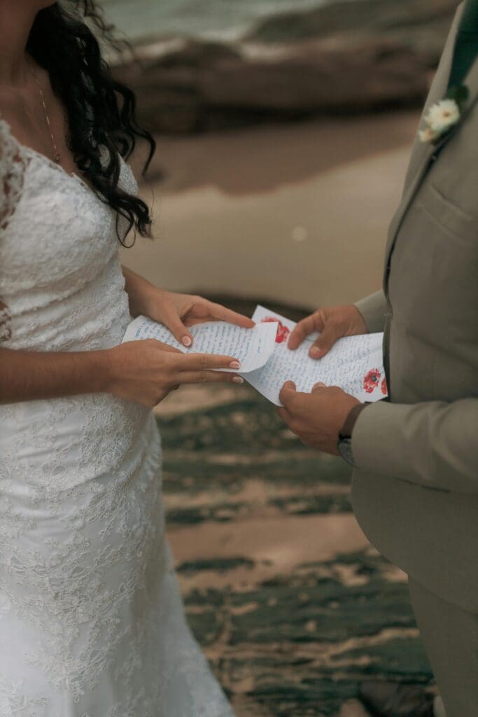 A close-up shot of the bride and groom exchanging handwritten wedding vows on a beach.