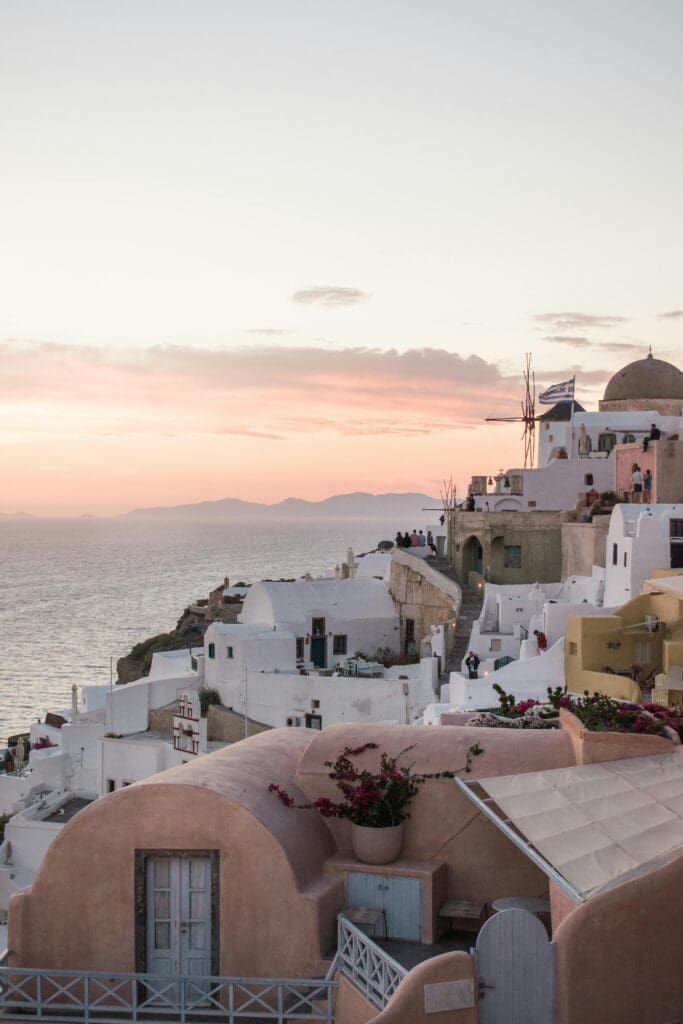 The iconic whitewashed buildings of Oia, Santorini, cascade down a cliffside at sunset, an idyllic backdrop for a luxury destination wedding.