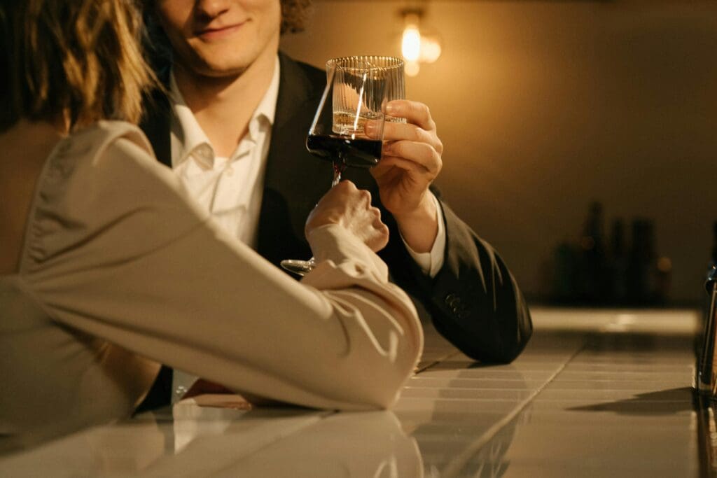 A sophisticated couple enjoys an intimate moment, clinking glasses of red wine at an exclusive, dimly lit cocktail bar.