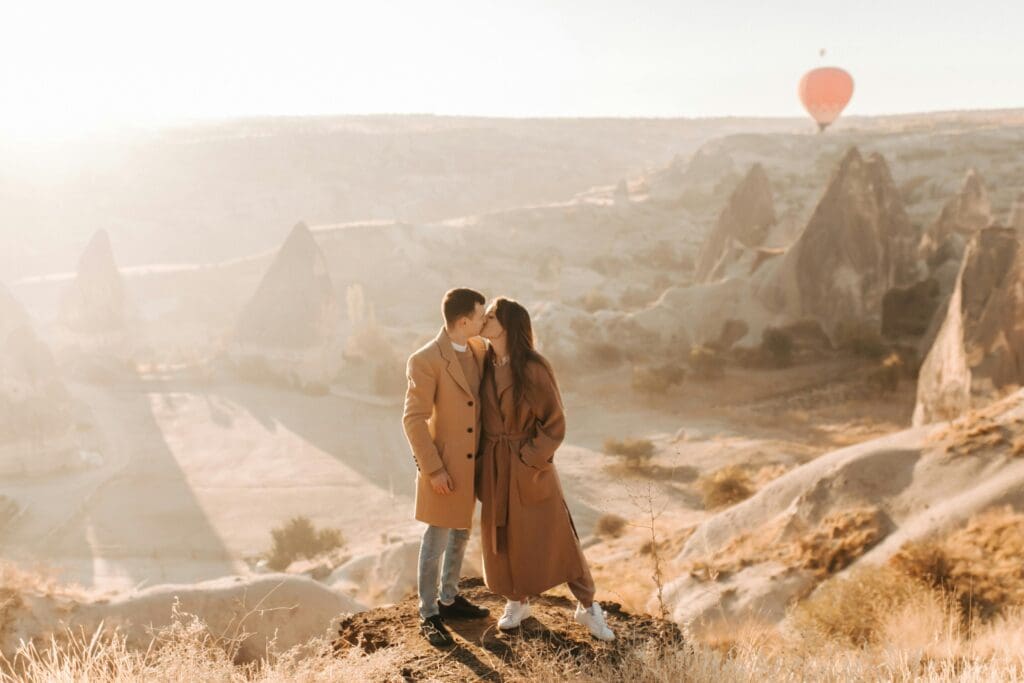 A couple on a romantic honeymoon in Cappadocia, Turkey, watches hot air balloons float over the rocky valleys at sunrise.