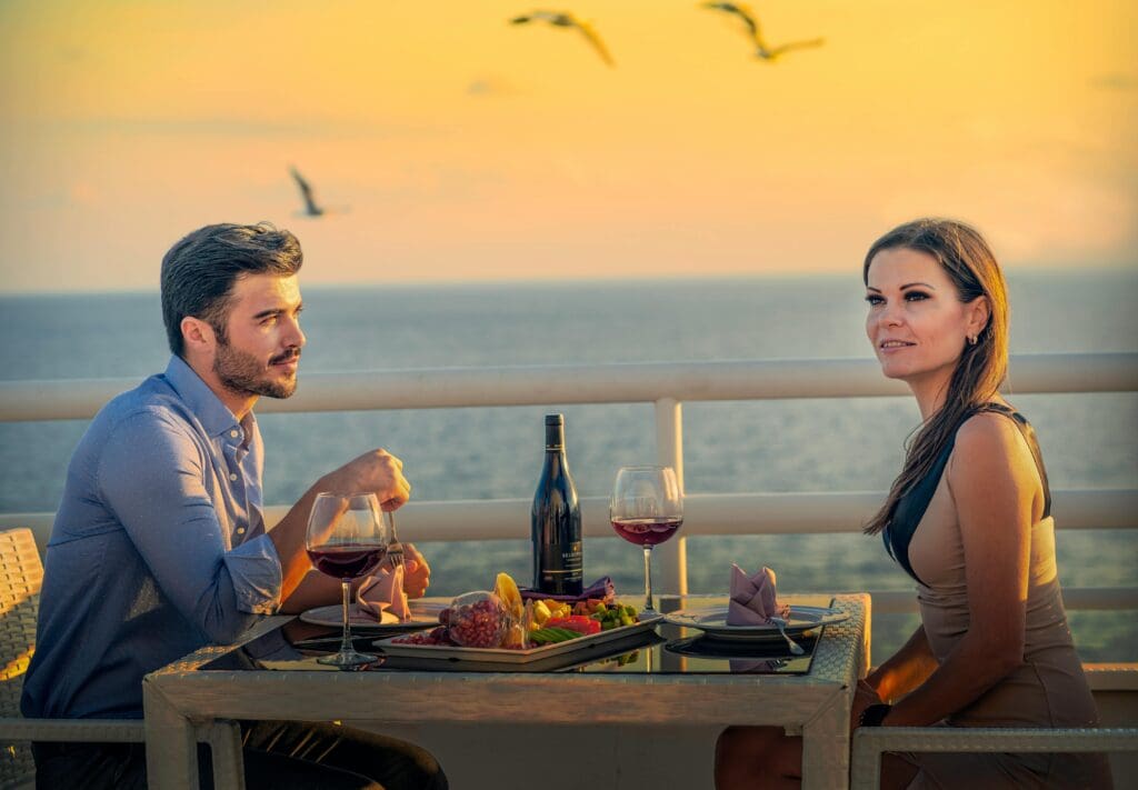 A couple enjoys a private, romantic dinner with wine on a luxury hotel balcony, overlooking a serene ocean at sunset.