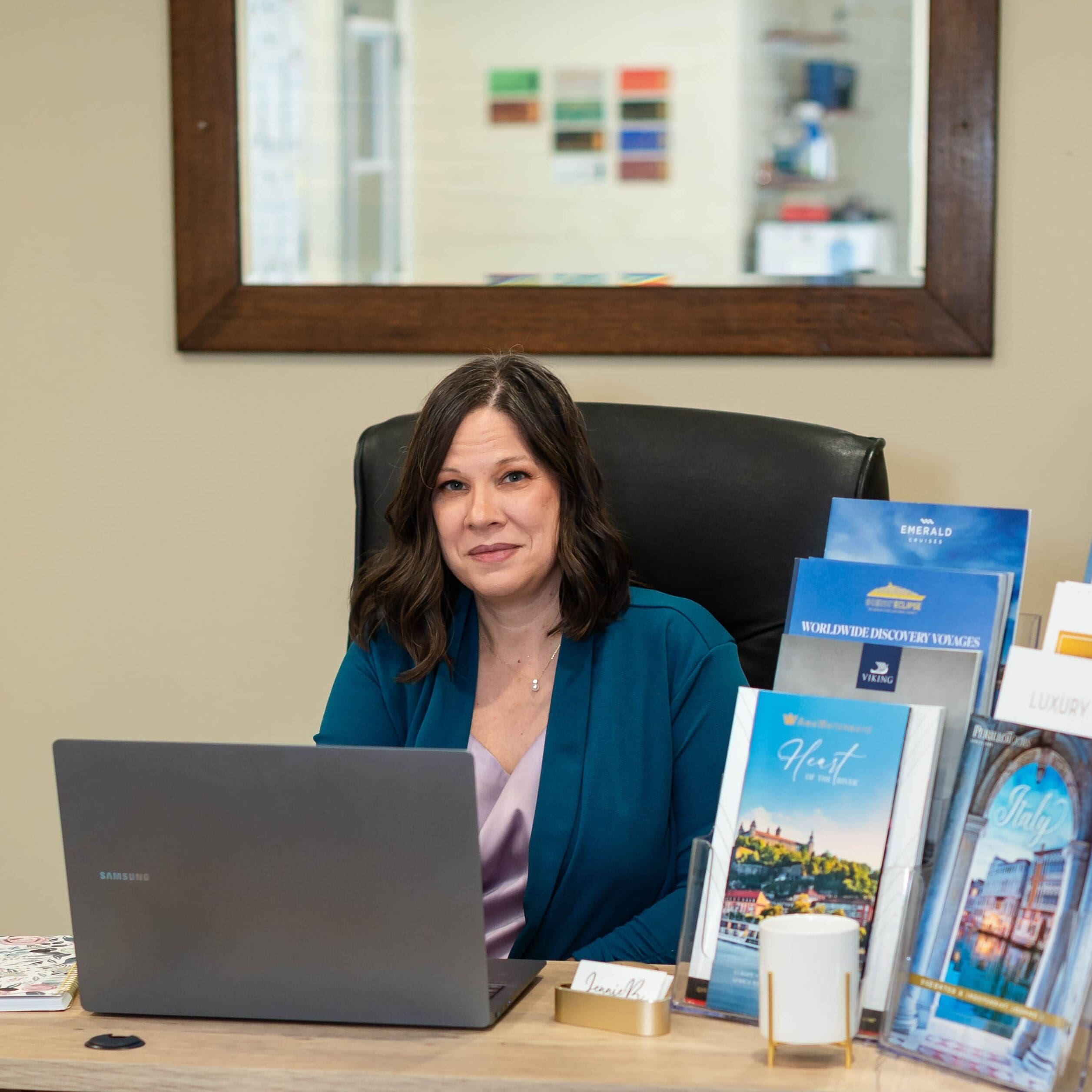 Jennie B, a professional travel advisor with 30 years of healthcare experience, sitting at an organized desk with travel brochures for Europe and cruises, providing expert vacation planning.